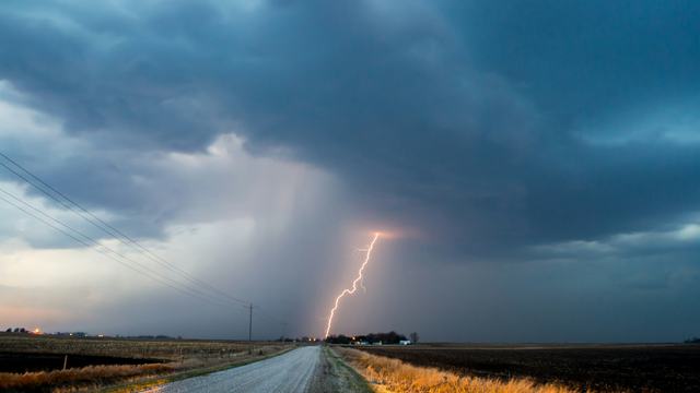 long stretch of road  with heavy  storm clouds and single lightening strike