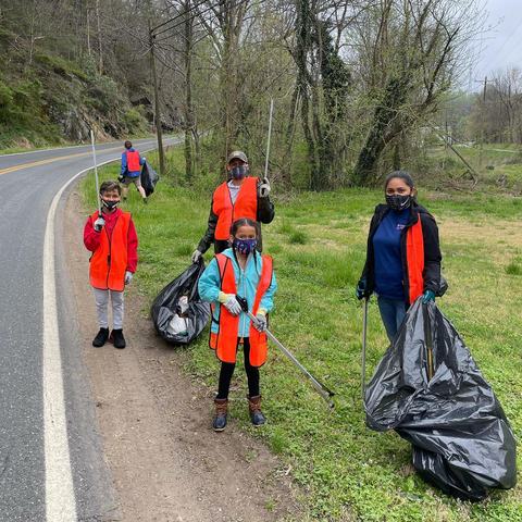 Family participating in a roadside clean up with trash bags and grabbers