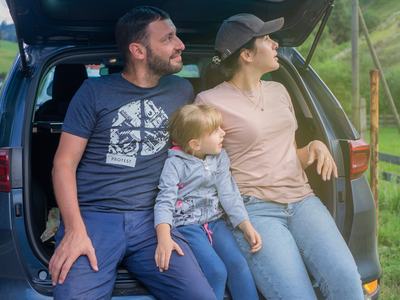 Two parents and child in middle sitting on tailgate of SUV.