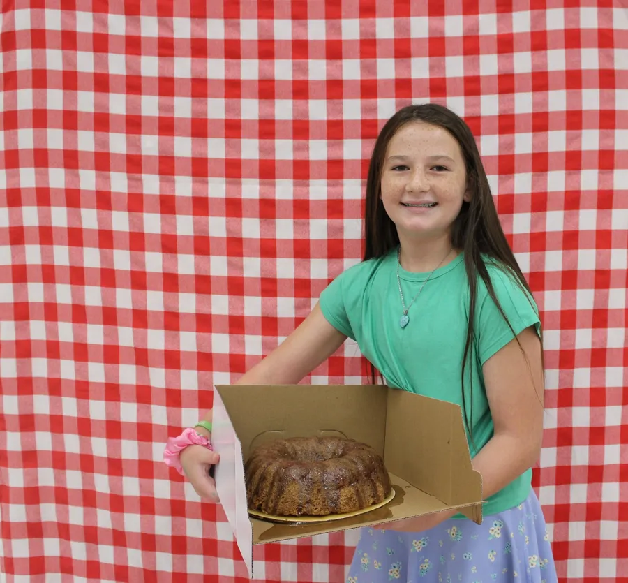 Girl stands in front of a red gingham background and smiles while holding a apple dish