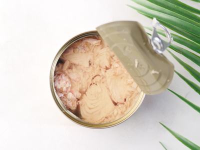 Open can of tuna on a light background with a decorative leaf.