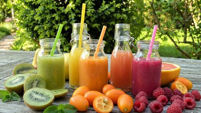 Gemini enhanced image of five colorful fruit smoothies in glass bottles, surrounded by fresh kiwi and berries