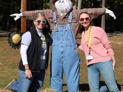 2 people posing with a scarecrow set up on the lawn