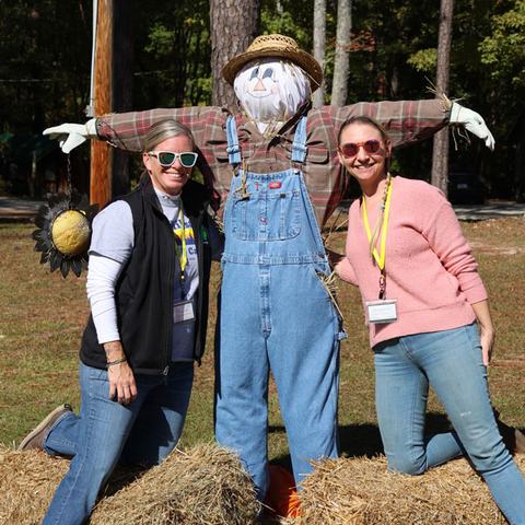 2 people posing with a scarecrow set up on the lawn
