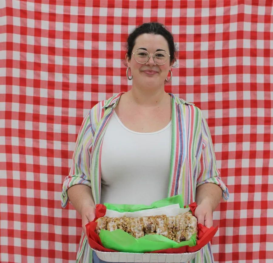 Woman stands in front of a red gingham background and smiles while holding a apple dish