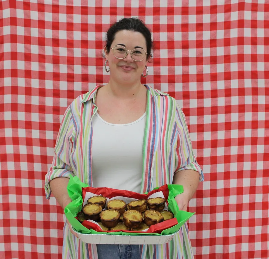 Woman stands in front of a red gingham background and smiles while holding a apple dish