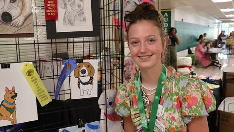 A 4-H member poses beside her award-winning artwork for the 4-H Dog Artistic Expression Contest displayed at the 2026 North Carolina 4-H State Presentation Finals.