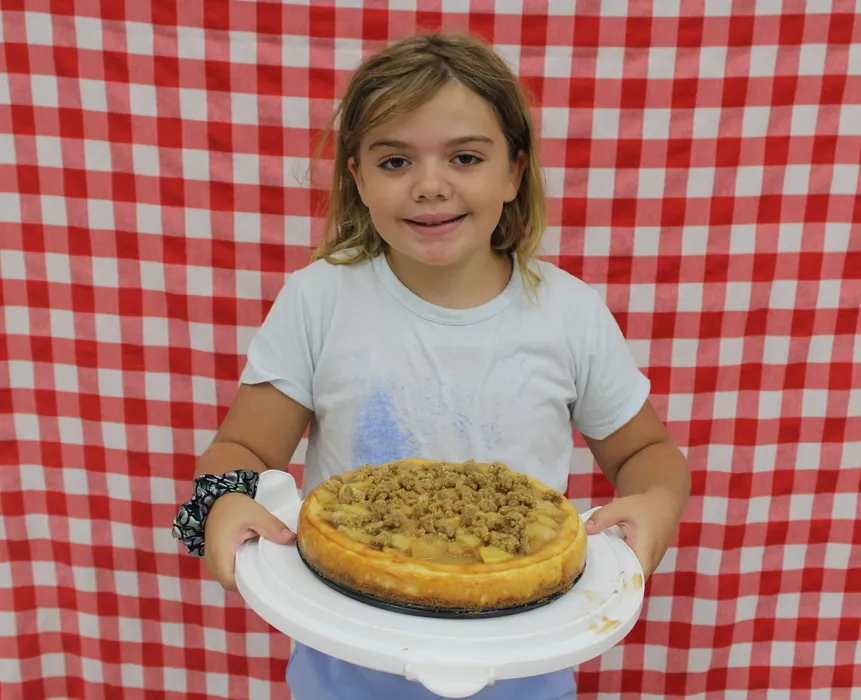 Girl stands in front of a red gingham background and smiles while holding a apple dish