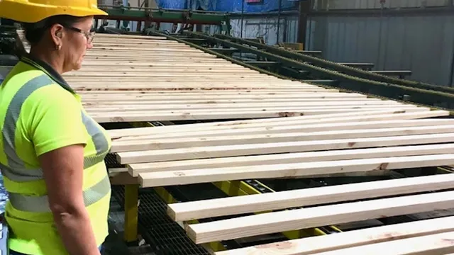 Mill worker in hard hat and safety vest inspecting lumber passing by on conveyor