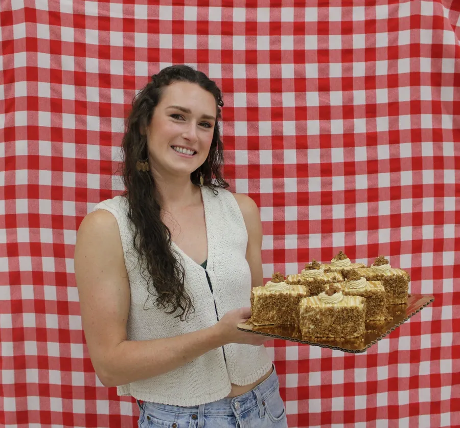 Woman stands in front of a red gingham background and smiles while holding a apple dish
