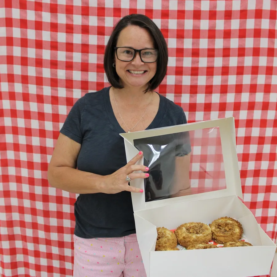 Woman stands in front of a red gingham background and smiles while holding a apple dish