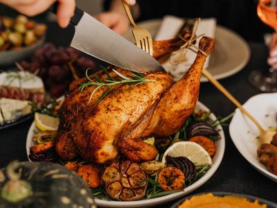 turkey on table being cut with knife and side dishes in the background