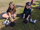 two 5th grade girls sitting in the grass smiling while playing in the compost samples