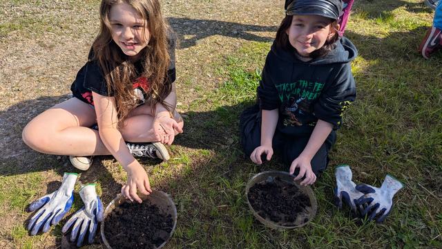 two 5th grade girls sitting in the grass smiling while playing in the compost samples