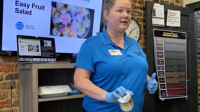 Jamie teaching a class in front of a screen while making a fruit salad