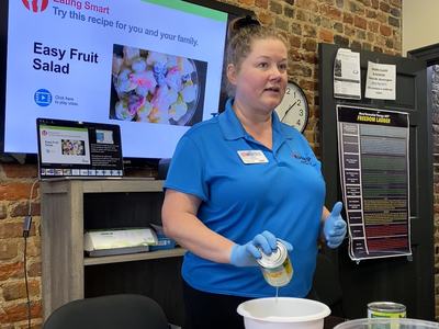 Jamie teaching a class in front of a screen while making a fruit salad